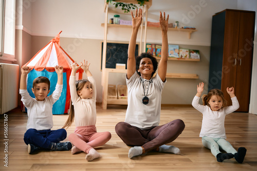 Happy black preschool teacher and group of kids stretching during exercise class. photo