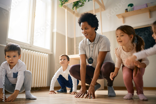 Happy African American PE teacher and group of kids having fun while exercising at kindergarten. photo