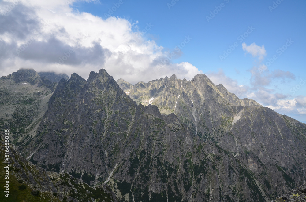 View to sharp rocky peaks covered low clouds of High Tatras mountains in Slovakia in summer. Trail to mount Slavkovsky stit View to sharp rocky peaks covered low clouds of High Tatras mountains in Slovakia in summer. Trail to mount Slavkovsky stit