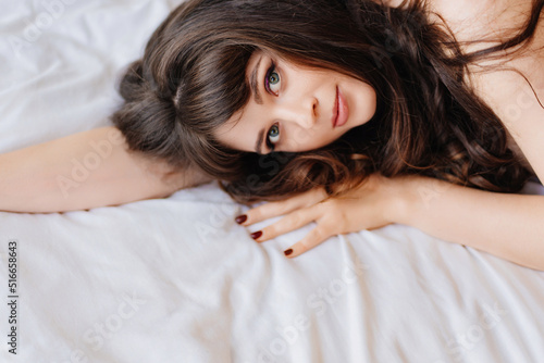 an attractive and sexy young woman with long dark hair lies in bed. bed linen.