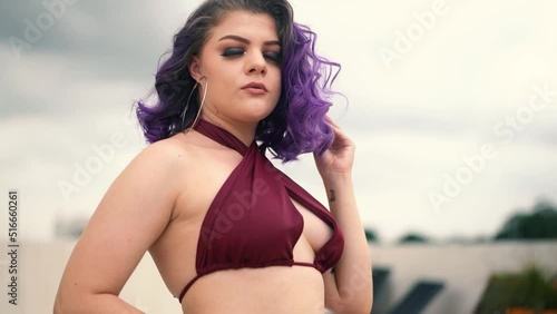 portrait of a young woman with purple hair posing on the roof of a building in a wine-colored bathing suit.  Slow motion 