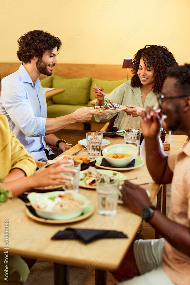 A small interracial group of friends is sitting in a restaurant and having dinner.
