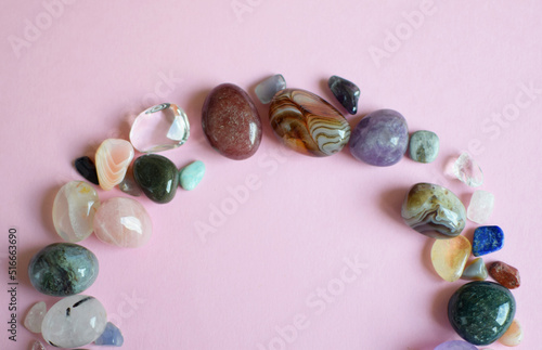 The circle is lined with natural minerals. Semi-precious stones of different colors, raw and processed. Amethyst, rose quartz, agate, apatite, aventurine on a pink background.