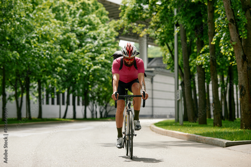 Fototapeta premium Strong Male cyclist in sportswear, glasses and protective helmet walking with his bike in the forest to take a break after riding. Sky blue and forest in the background.