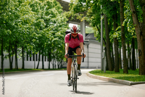 Strong Male cyclist in sportswear, glasses and protective helmet walking with his bike in the forest to take a break after riding. Sky blue and forest in the background.