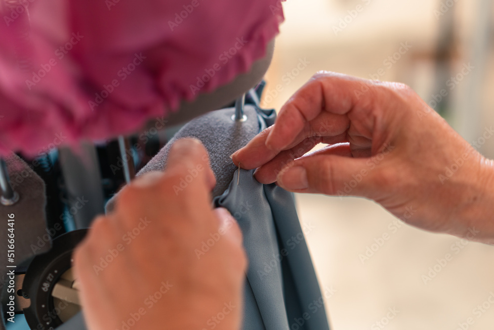 detail of the hands of a seamstress attaching a garment to a mannequin with a pin