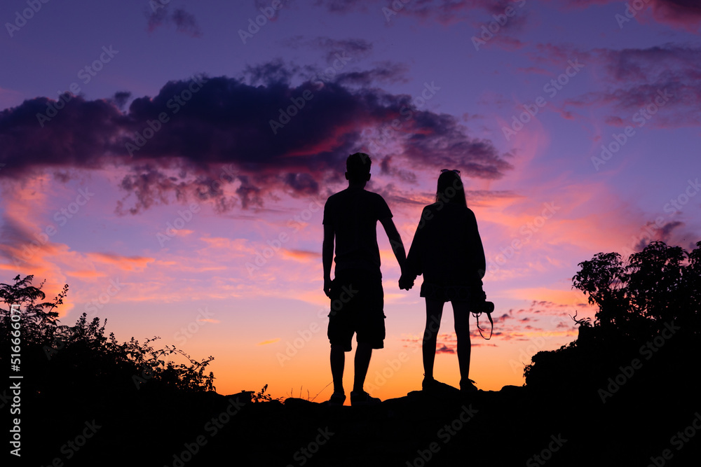 Silhouette of couple holding hands and watching a colourful sunset together