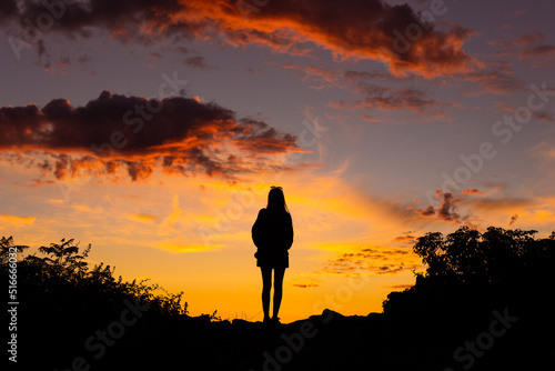 Fototapeta Naklejka Na Ścianę i Meble -  Silhouette of woman with camera standing on hilltop watching sunset