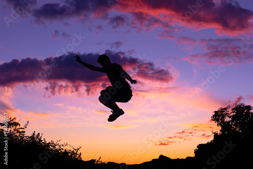 Silhouette of man jumping in the air against a colourful sunset background