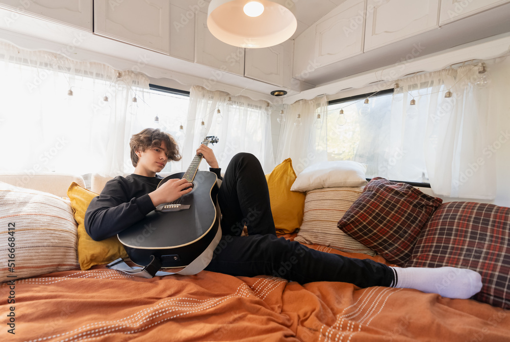 Fototapeta premium young guy plays the guitar lying on the bed in a camper van.