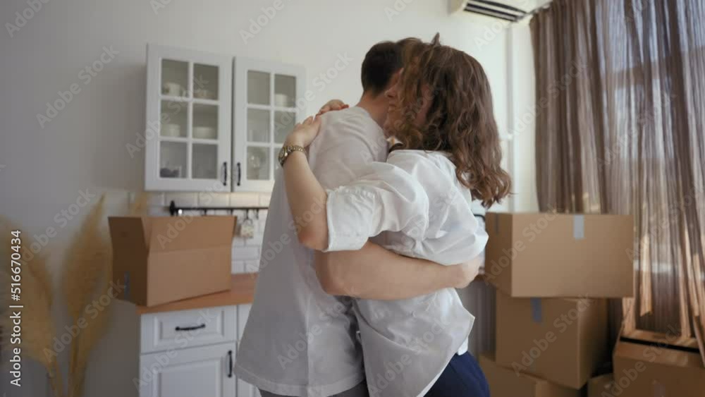 Man spins woman around and hugs in modern kitchen of new apartment against unpacked paper boxes. Happy young couple feels excited about relocation Man spins woman around and hugs in modern kitchen of new apartment against unpacked paper boxes. Happy young couple feels excited about relocation