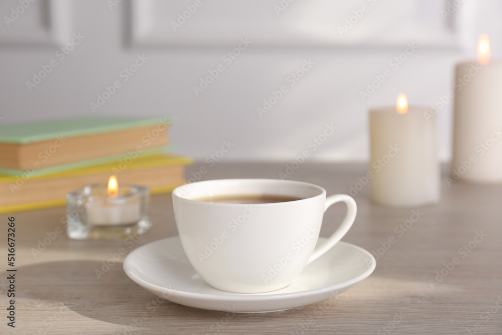 Cup of aromatic coffee and burning candles on wooden table indoors Cup of aromatic coffee and burning candles on wooden table indoors