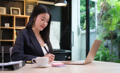 Beautiful businesswoman working with computer laptop and writing notes on notebook.