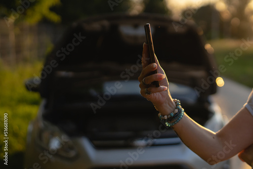 side view of hand of unknown caucasian woman holding mobile phone against opened car hood broken failed engine roadside assistance and towing service concept copy space