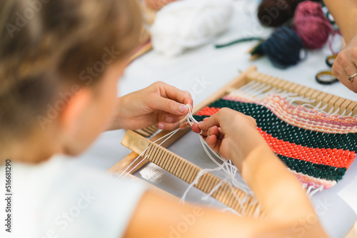 Girl weaving small rug with pattern at masterclass on weaving. Girl is studying how to weave on manual table loom. Process of creation. Handmade concept