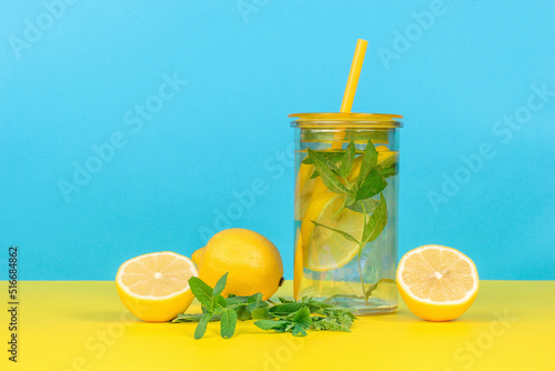 Water with lemon and mint in a glass on a yellow and blue background.