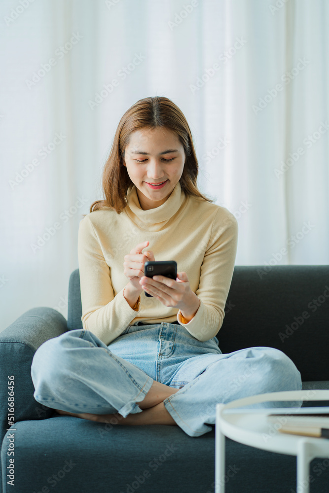 Attractive Asian woman relaxing on the sofa Use your smartphone to surf the internet, work online at home, and shop online. Attractive Asian woman relaxing on the sofa Use your smartphone to surf the internet, work online at home, and shop online.