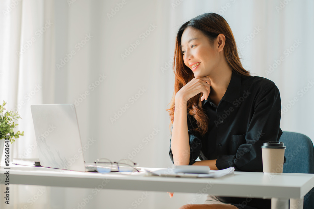 Smiling happy Asian woman relaxing using the technology of a laptop computer while sitting in a chair at a desk. creative girl working at home The concept of working and studying online learning Smiling happy Asian woman relaxing using the technology of a laptop computer while sitting in a chair at a desk. creative girl working at home The concept of working and studying online learning