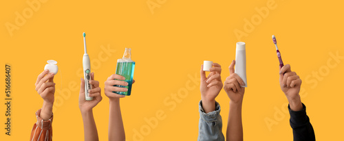 Many hands with toothbrushes, paste, mouth rinse and dental floss on yellow background