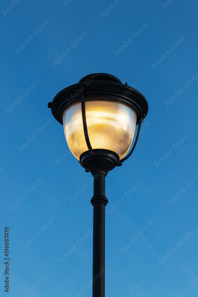 Glowing street lamp is under deep blue sky, close up