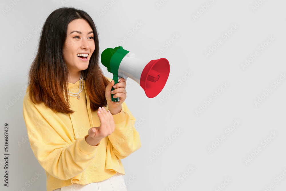 Young Asian woman with megaphone on light background. Concept of studying Italian language Young Asian woman with megaphone on light background. Concept of studying Italian language