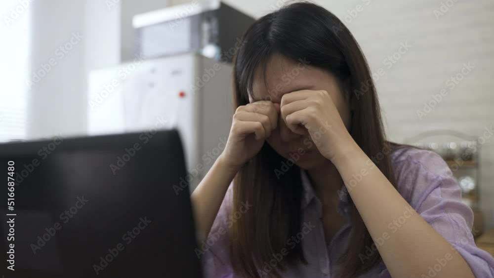 slow motion overworked asian businesswoman is trying to relieve her blurred vision with massage and squinting at the computer screen while working from home. slow motion overworked asian businesswoman is trying to relieve her blurred vision with massage and squinting at the computer screen while working from home.