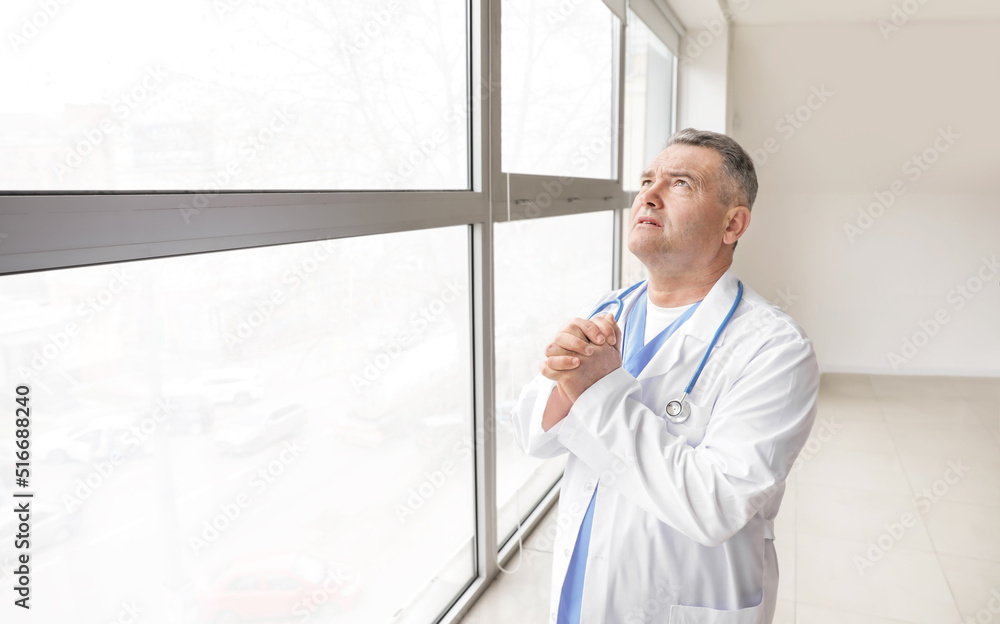 Praying mature male doctor in clinic Praying mature male doctor in clinic