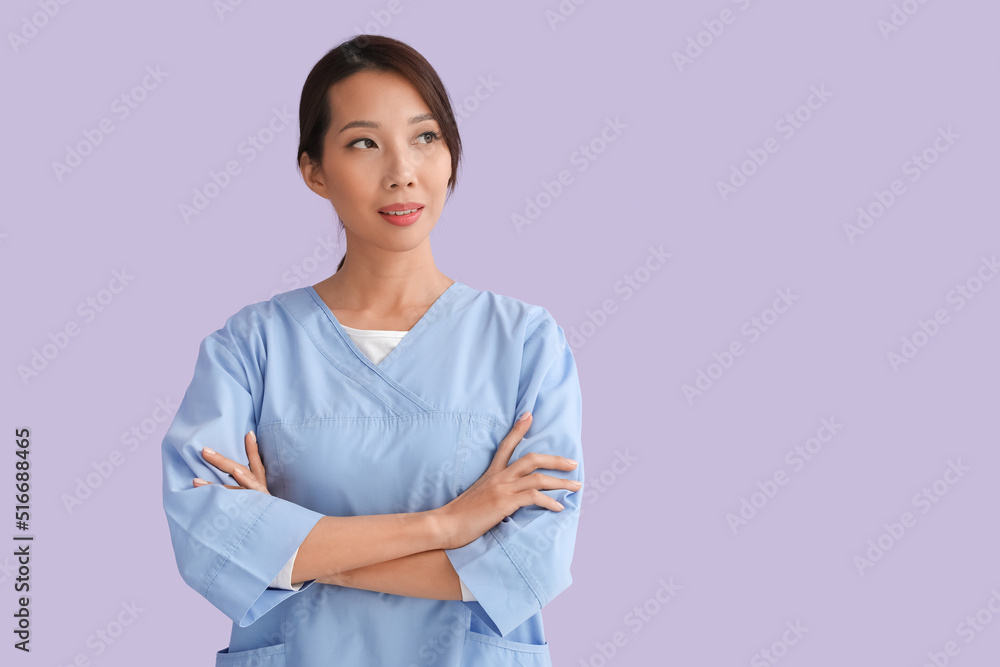 Female Asian nurse with crossed arms on lilac background Female Asian nurse with crossed arms on lilac background