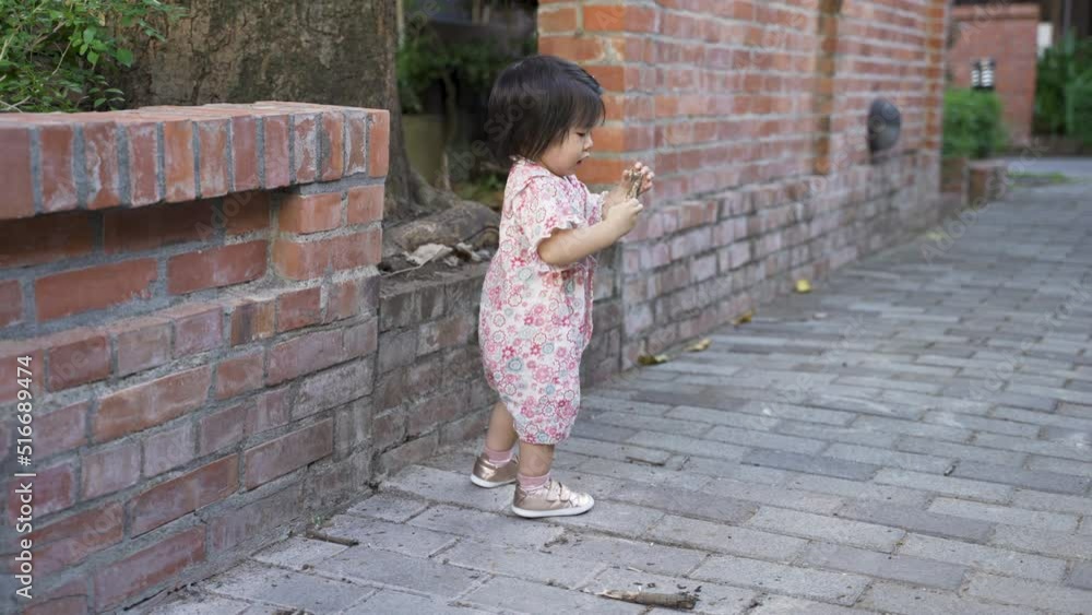 full length shot of a cute toddler kid in japanese kimono is showing the bark in hand to someone at distance while playing in a cultural park by red brick wall. full length shot of a cute toddler kid in japanese kimono is showing the bark in hand to someone at distance while playing in a cultural park by red brick wall.
