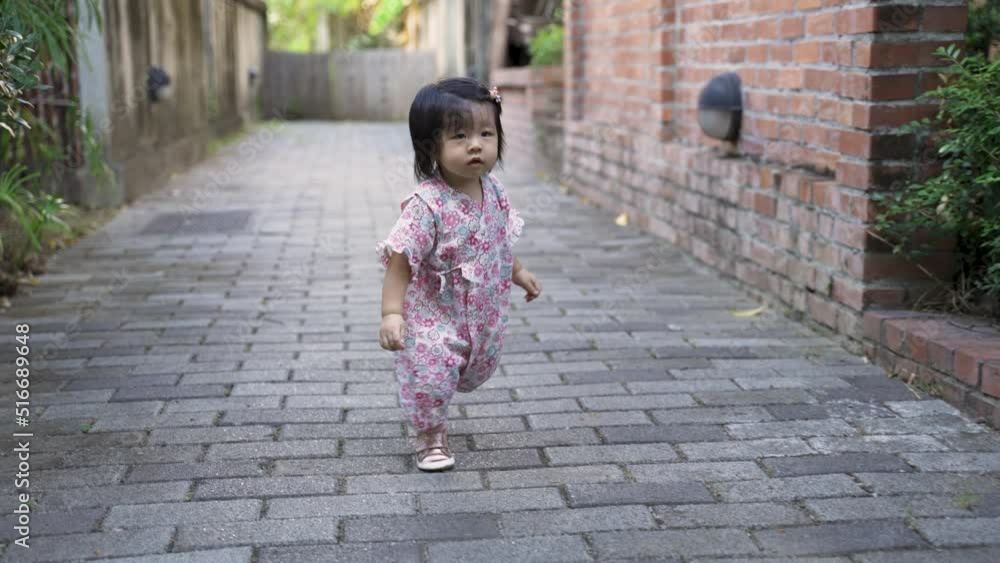 front view with full length shot cute toddler girl learning to walk in kimono is smiling with innocence as she is waddling along and nearly tripped on brick path front view with full length shot cute toddler girl learning to walk in kimono is smiling with innocence as she is waddling along and nearly tripped on brick path