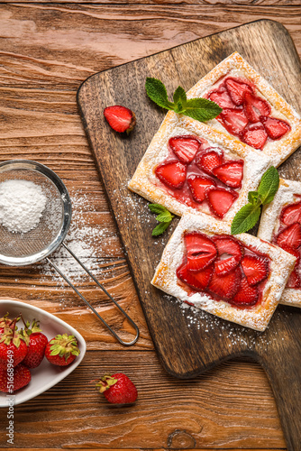 Delicious strawberry puff pastry and sieve with sugar powder on wooden background, closeup