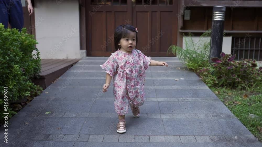 slow motion of an energetic japanese baby toddler wearing kimono is freed from mother and waddling down a slope out of gate from her traditioanl house building.
