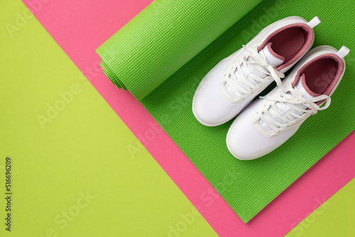 Fitness concept. Top view photo of white sneakers over sports mat on bicolor green and pink background with copyspace