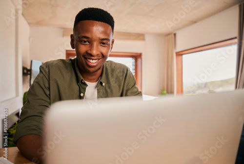 Close up portrait of a happy Young adult black African-American male smiling while using his laptop. Remote working from his modern apartment photo
