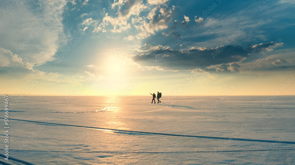 Fototapeta premium The couple of travelers walking through the snow field on sunset background
