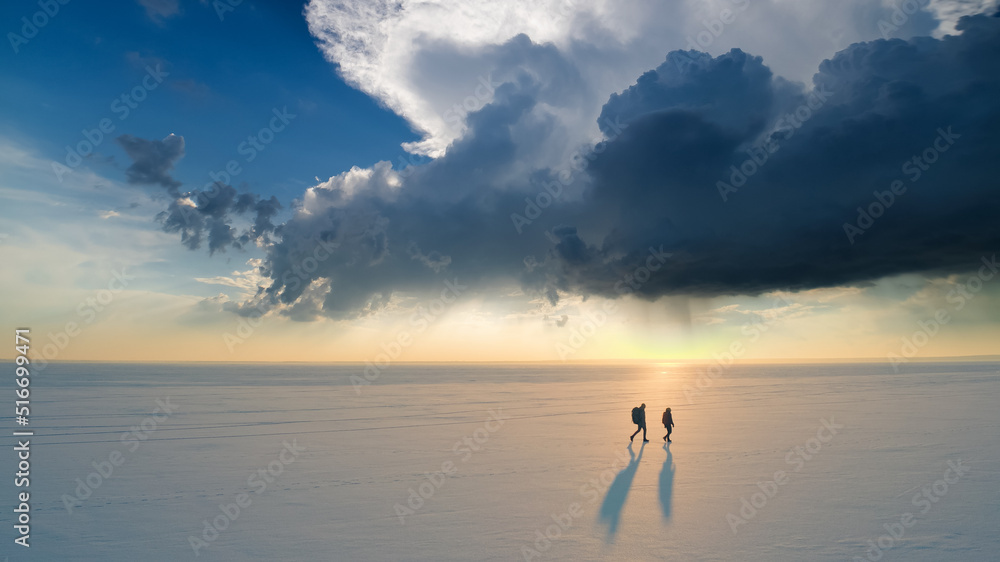 The two tourists going through the snow field against beautiful sky