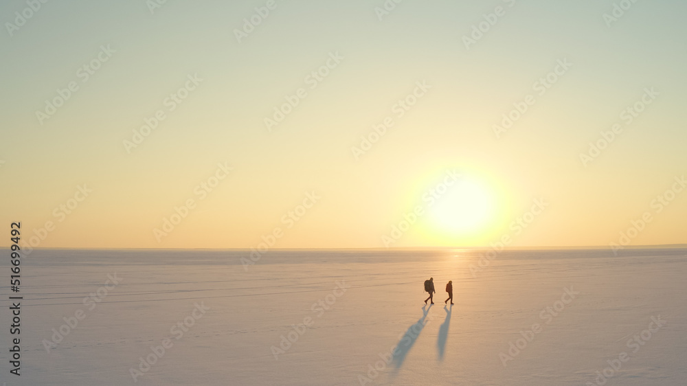The two people with backpacks going through the snow field against beautiful sky