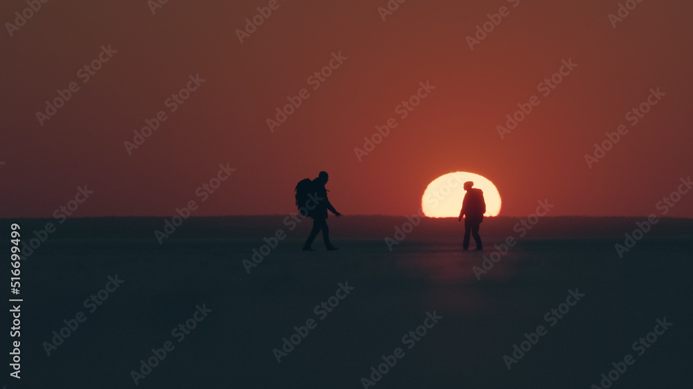 The two travelers standing through the snow field against beautiful sunset