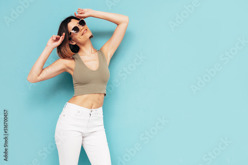 Young beautiful smiling female in trendy summer jeans clothes. Carefree woman posing near blue wall in studio. Sexy positive model having fun indoors. Cheerful and happy. Isolated. In sunglasses © halayalex