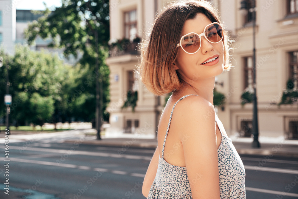 Young beautiful smiling hipster woman in trendy summer dress clothes. Sexy carefree model posing on the street background at sunset. Positive brunette female. Cheerful and happy. In sunglasses