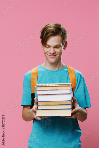 red-haired young man student stands with textbooks in his hands and looks pleasantly smiling at his books