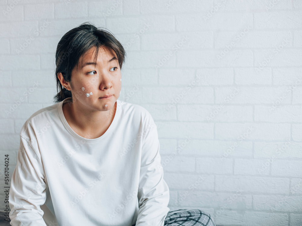 teenage girl with problematic skin, with a therapeutic cream applied. white brick wall background