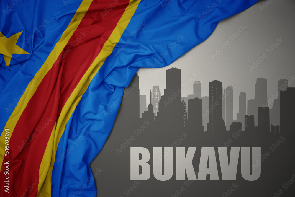 abstract silhouette of the city with text Bukavu near waving colorful national flag of democratic republic of the congo on a gray background.
