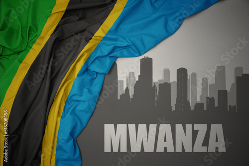 abstract silhouette of the city with text Mwanza near waving colorful national flag of tanzania on a gray background. photo