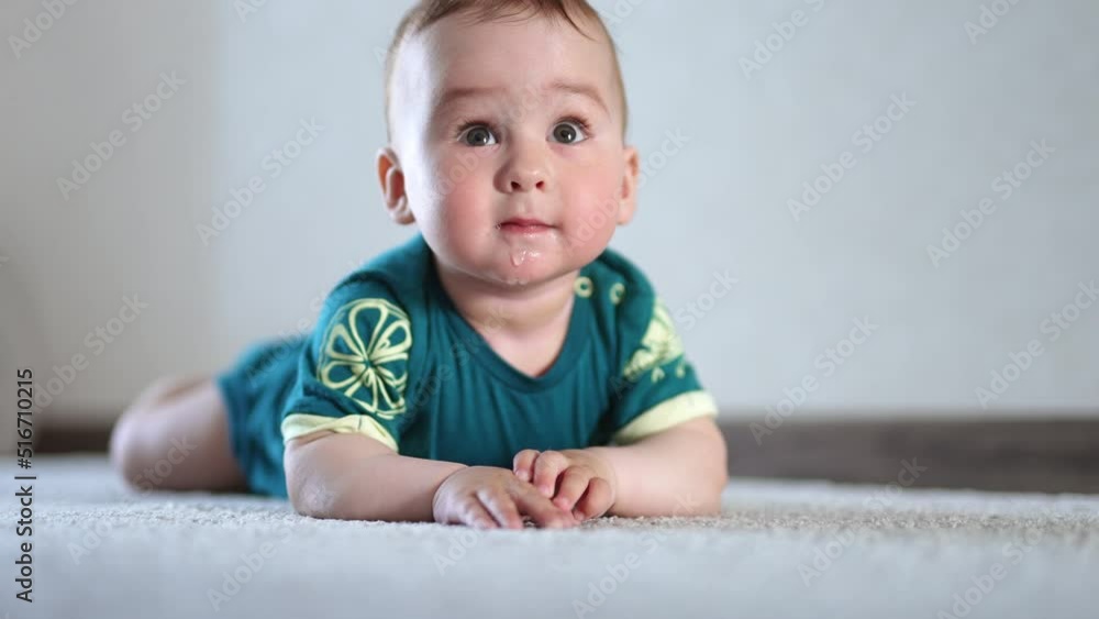 Cute active kid clapping hands by the floor. Baby lies on the carpet and looks around with interest and curiosity. Cute active kid clapping hands by the floor. Baby lies on the carpet and looks around with interest and curiosity.