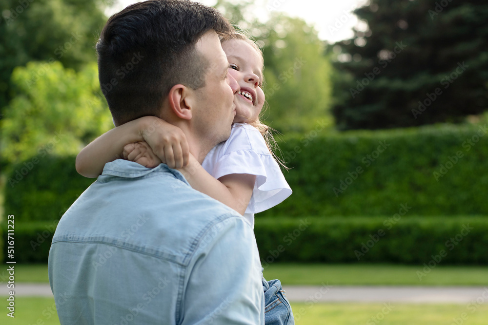 A family. Dad holds his daughter in his arms and hugs tightly in the park in the summer. A family. Dad holds his daughter in his arms and hugs tightly in the park in the summer.