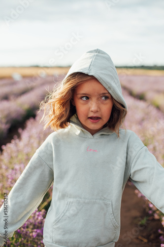 pretty 6 year old girl in mint hoodie with cute hairstyle in motion among lavender field in morning light