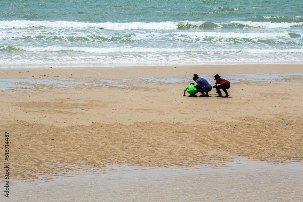 Girls and boys strolling on the sandy beach into the sea for a walk, the sea among the waves and the wind on a sunny and bright day is a peaceful sight in the background overlooking the sea.