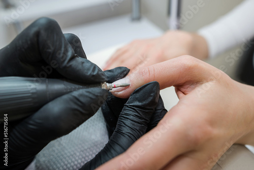 Professional hardware manicure on an electric machine in a nail salon. The process of lifting the cuticle with a cutter close-up.