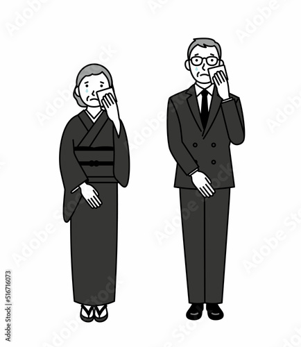 涙を拭く喪服のシニア男女